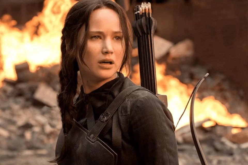 Personagem Katniss Evergreen próxima a um prédio derrubado em chamas no terceiro filme da trilogia "Jogos Vorazes".