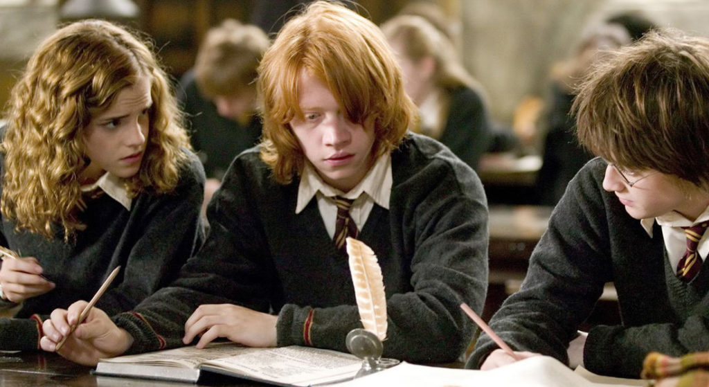 Personagens Harry Potter, Hermione Granger e Ron Weasley sentados em uma mesa no terceiro filme da franquia "Harry Potter e o Cálice de fogo".